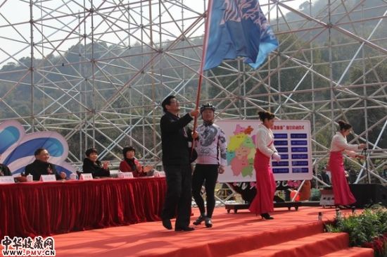 杭州市政府副市长张建庭（左）给杭州环超山自行车骑游队代表授旗