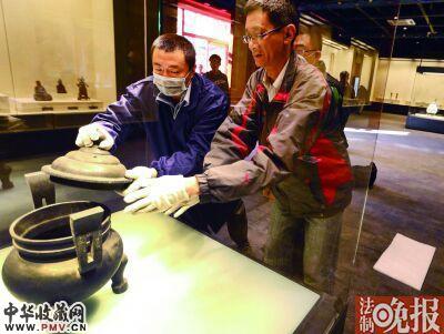工作人员将清双天官帽耳带盖蹄足铜炉放置在展台上